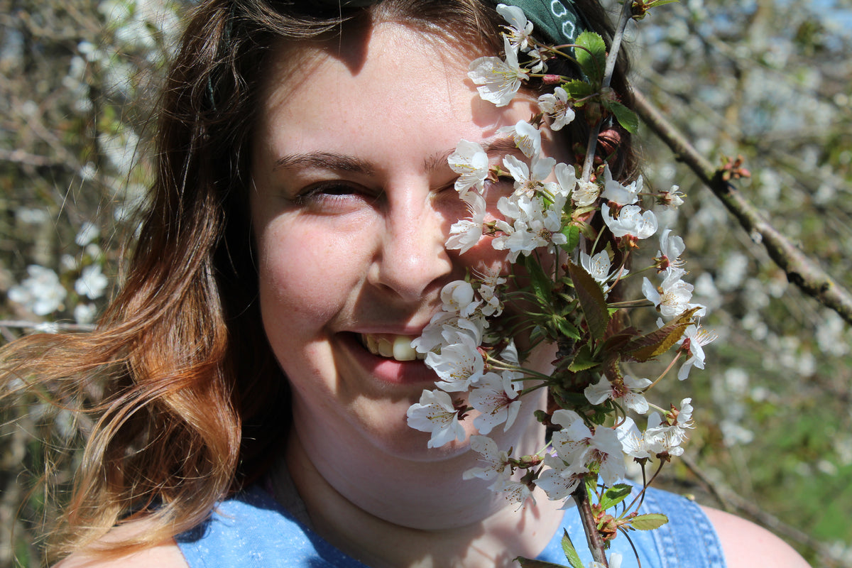 Photograph of the artist Emma-Leigh behind tree blossom.