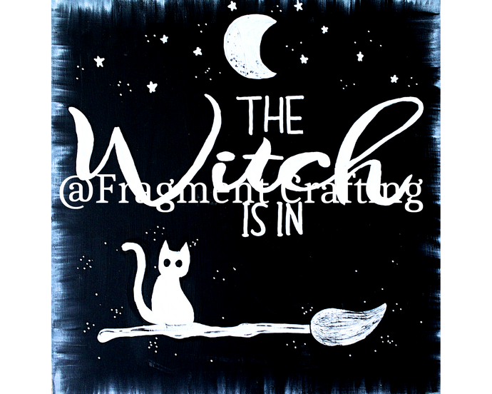 A print copy of  a black background with white moon and stars and cat sitting on a broom with the title The Witch Is in.