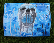 Load image into Gallery viewer, A print copy on the grass of Aquarius star sign painting of blue background and white skull with open mouth.
