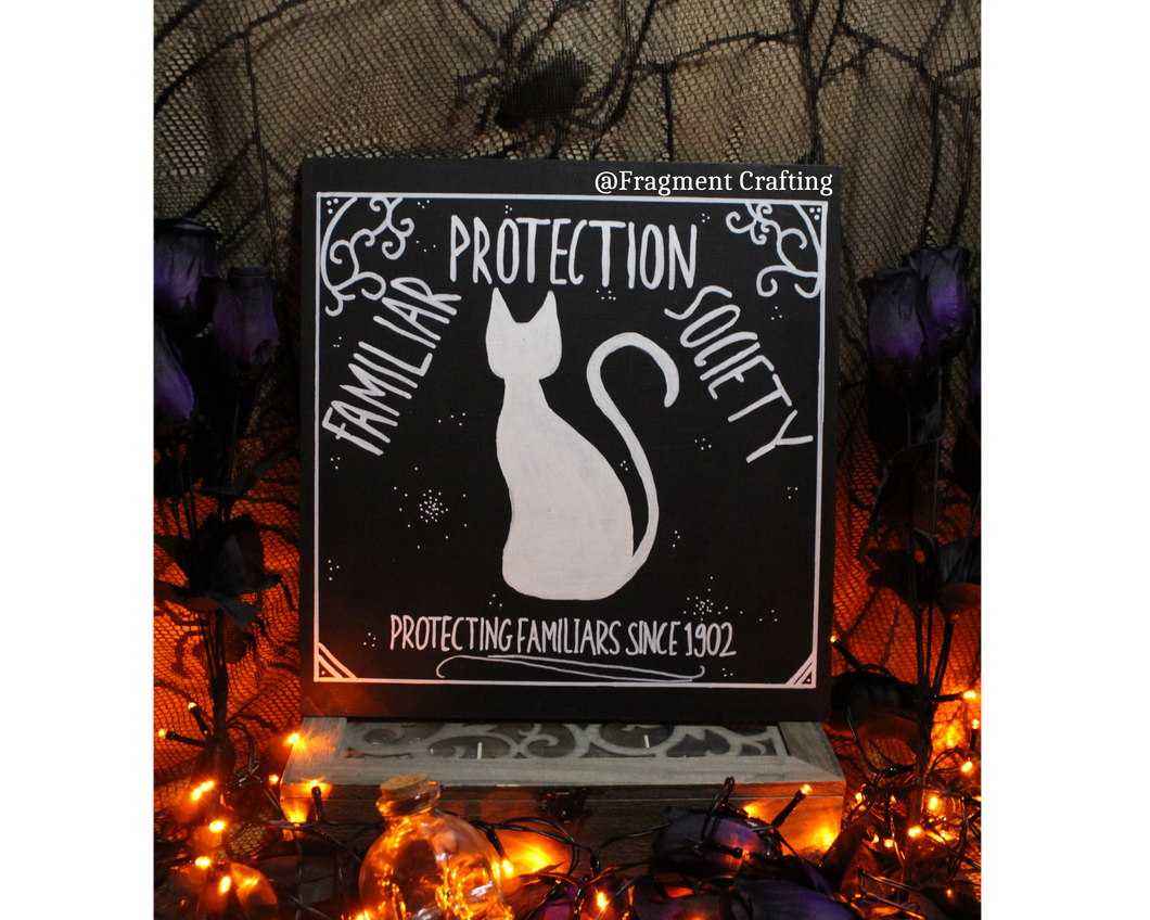 A wooden sign of a black background with a white silhouette of a cat with title of Familiar Protection Society Protecting Familiars since 1902 being showed in a Halloween setting.