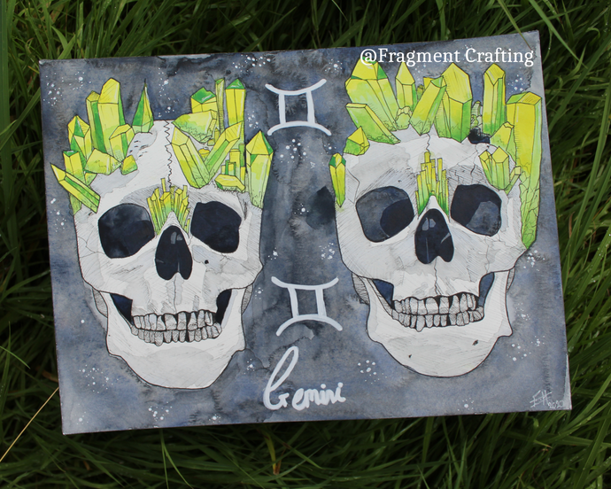 An original watercolour painting of the zodiac Gemini star sign of two skulls on a grey background being shown off on grass.