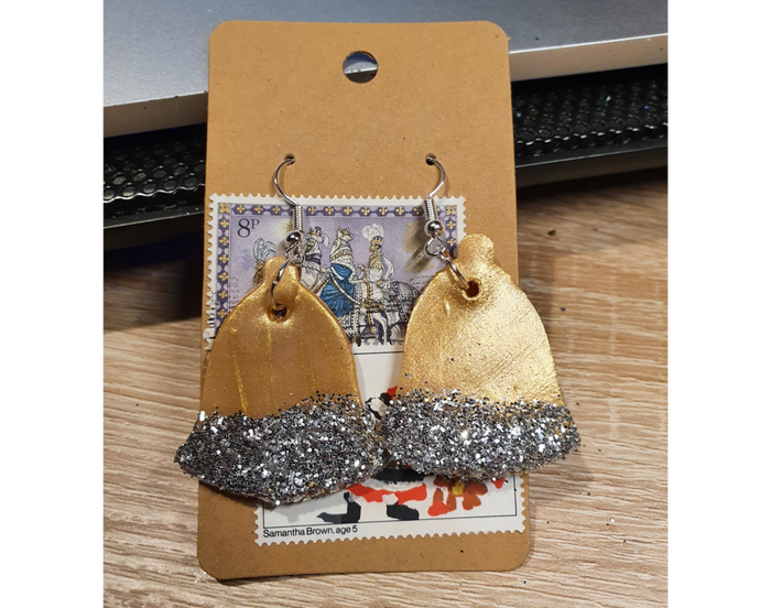 A pair of clay gold bell earrings and silver hooks and with silver glitter decoration.