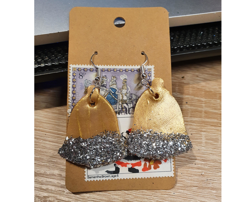 A pair of clay gold bell earrings and silver hooks and with silver glitter decoration.