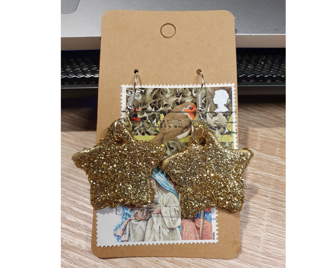 A pair of gold glittery star earrings with silver hooks.