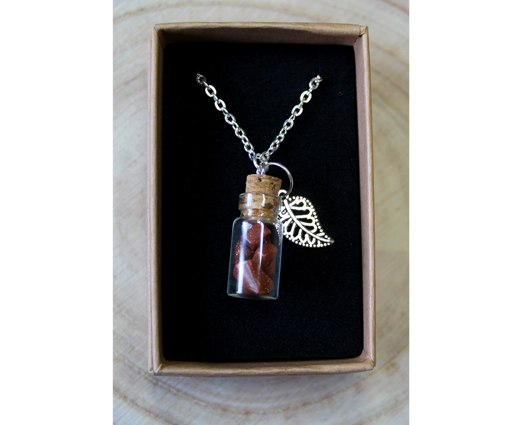 A boxed silver necklace with a leaf and small corked bottle of goldstone crystals.