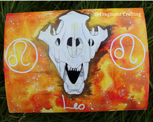 Load image into Gallery viewer, A print copy of a Leo star sign watercolour painting with a yellow and orange background and white skull of a lion being showed off on the grass.
