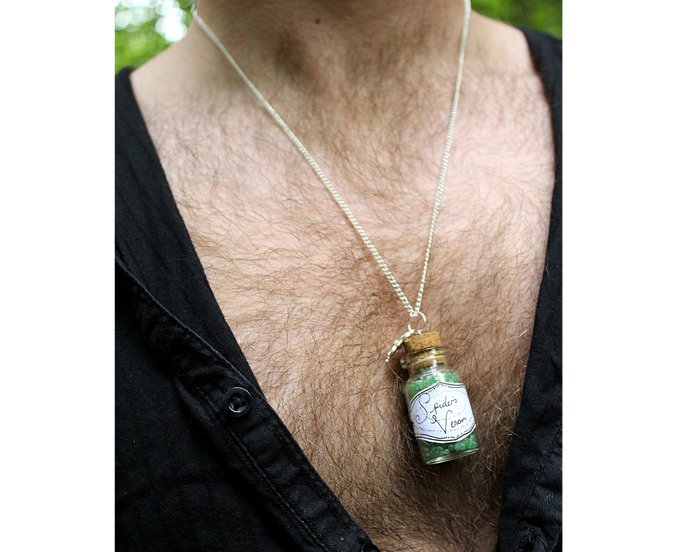 A man wearing a silver necklace with a leaf and small corked bottle of green crystals with the bottle labelled Spider's Venom.