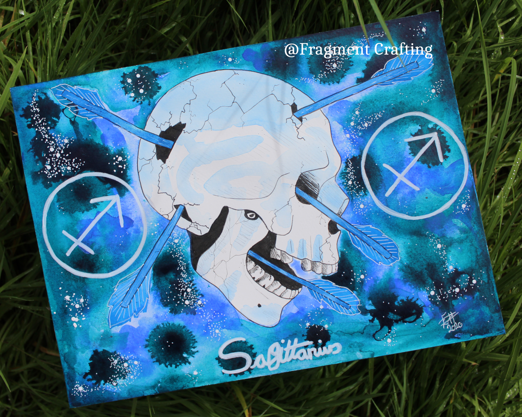 An original watercolour painting of the zodiac Sagittarius star sign of a white skull with arrows through on a blue background being showcased on the grass.