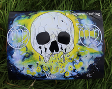 Load image into Gallery viewer, A print copy of a Virgo star sign watercolour painting with a black, grey and yellow background and white broken skull being showcased on the grass.
